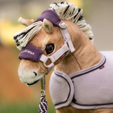 Brown toy pony wears a headcollar in lilac on a blurred outdoor background